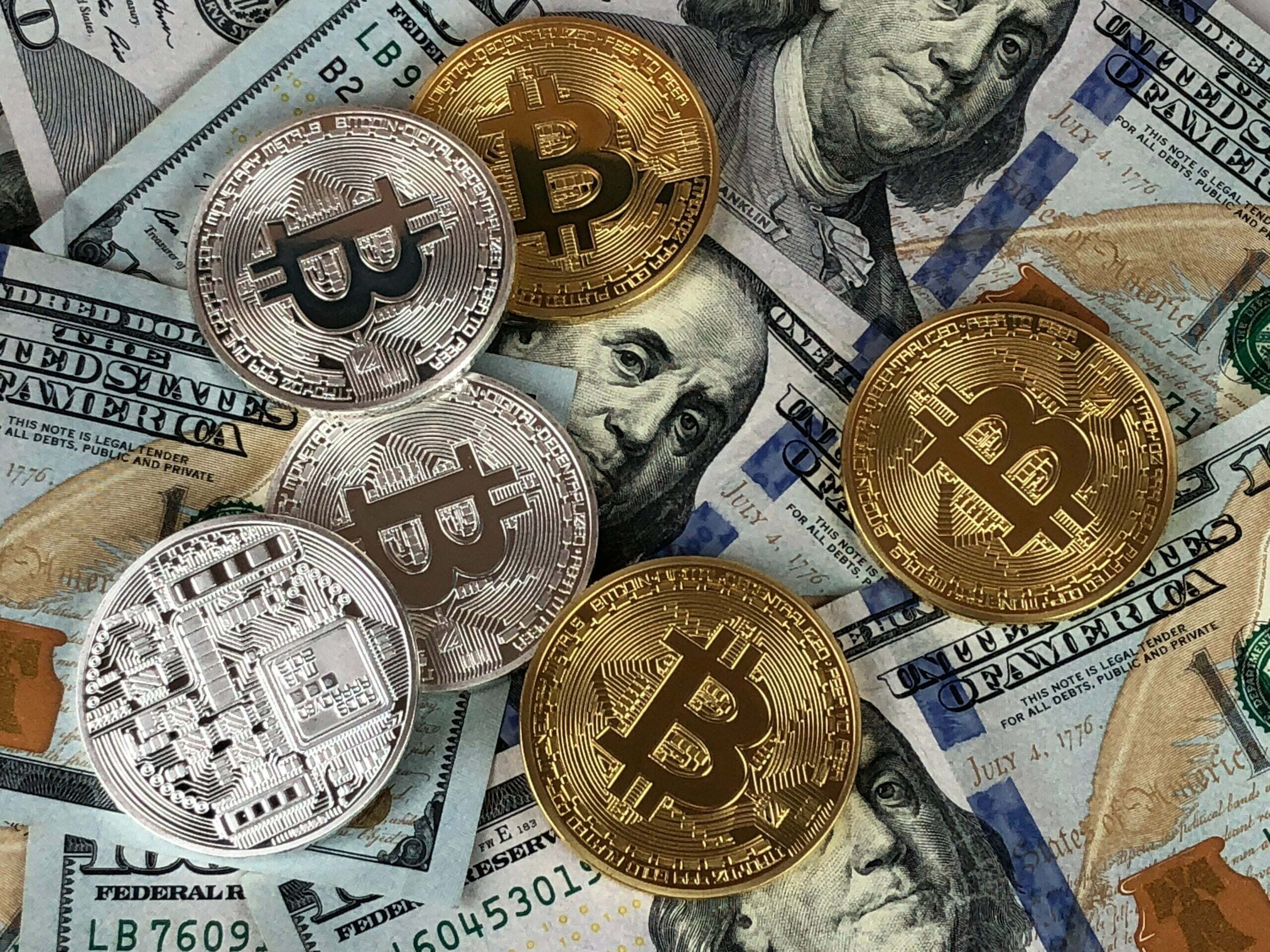 Monety z wizerunkiem Bitcoina na tle banknotów dolarowych
