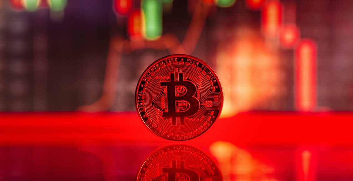 Zdjęcie czerwonej monety Bitcoina na tle świec i wykresów