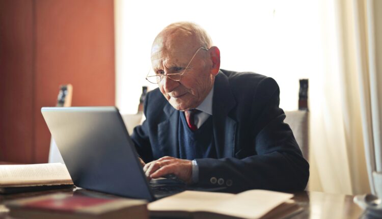 Emeryt w garniturze siedzący przed laptopem
