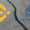 rozszczepiony beton z logiem binance i interpol po każdej ze stron