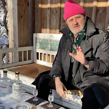 Palikot siedzi na ławce ubrany w kurtkę i testuje alkohole w zimowej aurze, przed domem