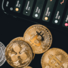 Monety kryptowalutowe oraz smartfon z kursami tych kryptowalut na czarnym tle