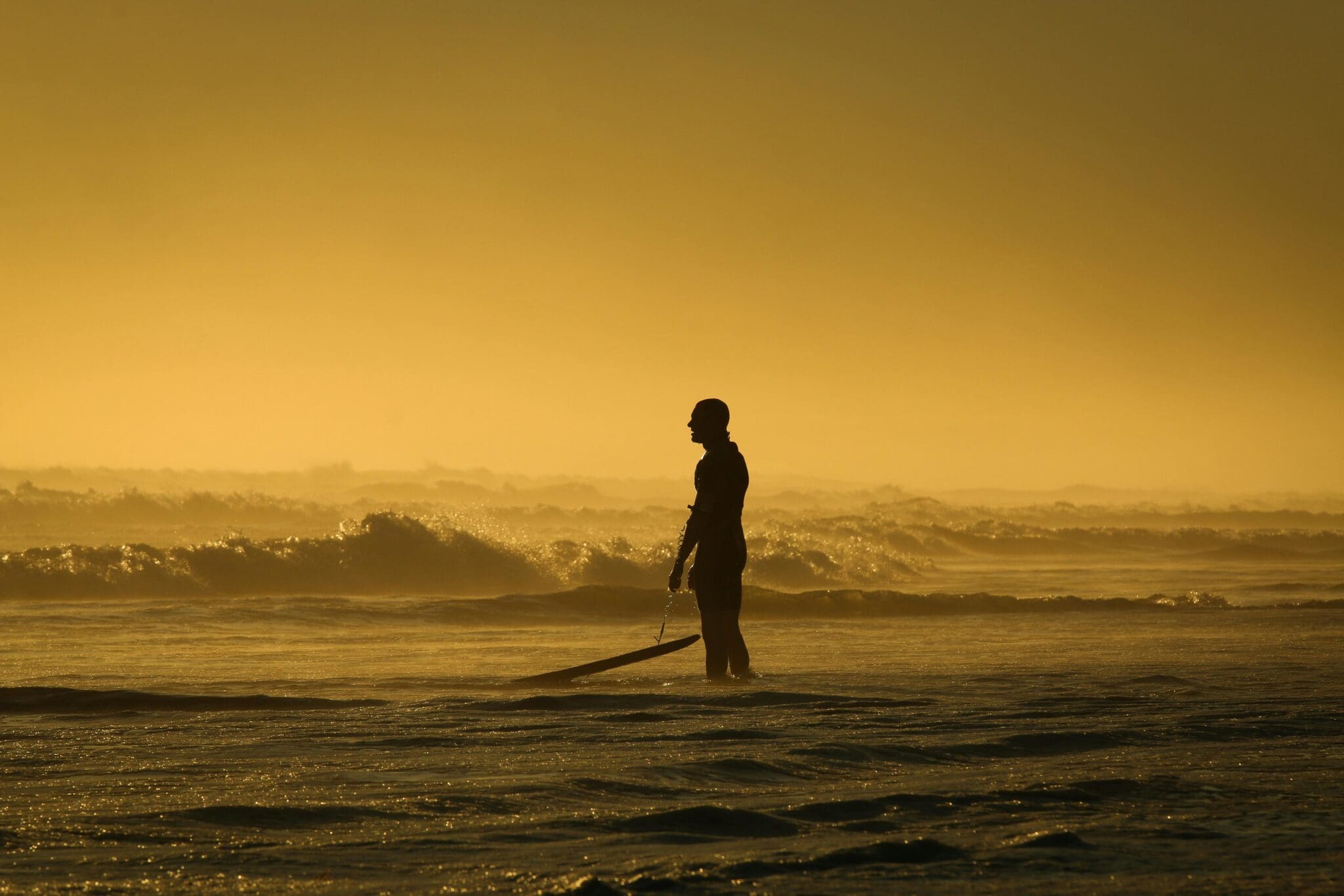 Samotny surfer na plaży o zachodzie słońca