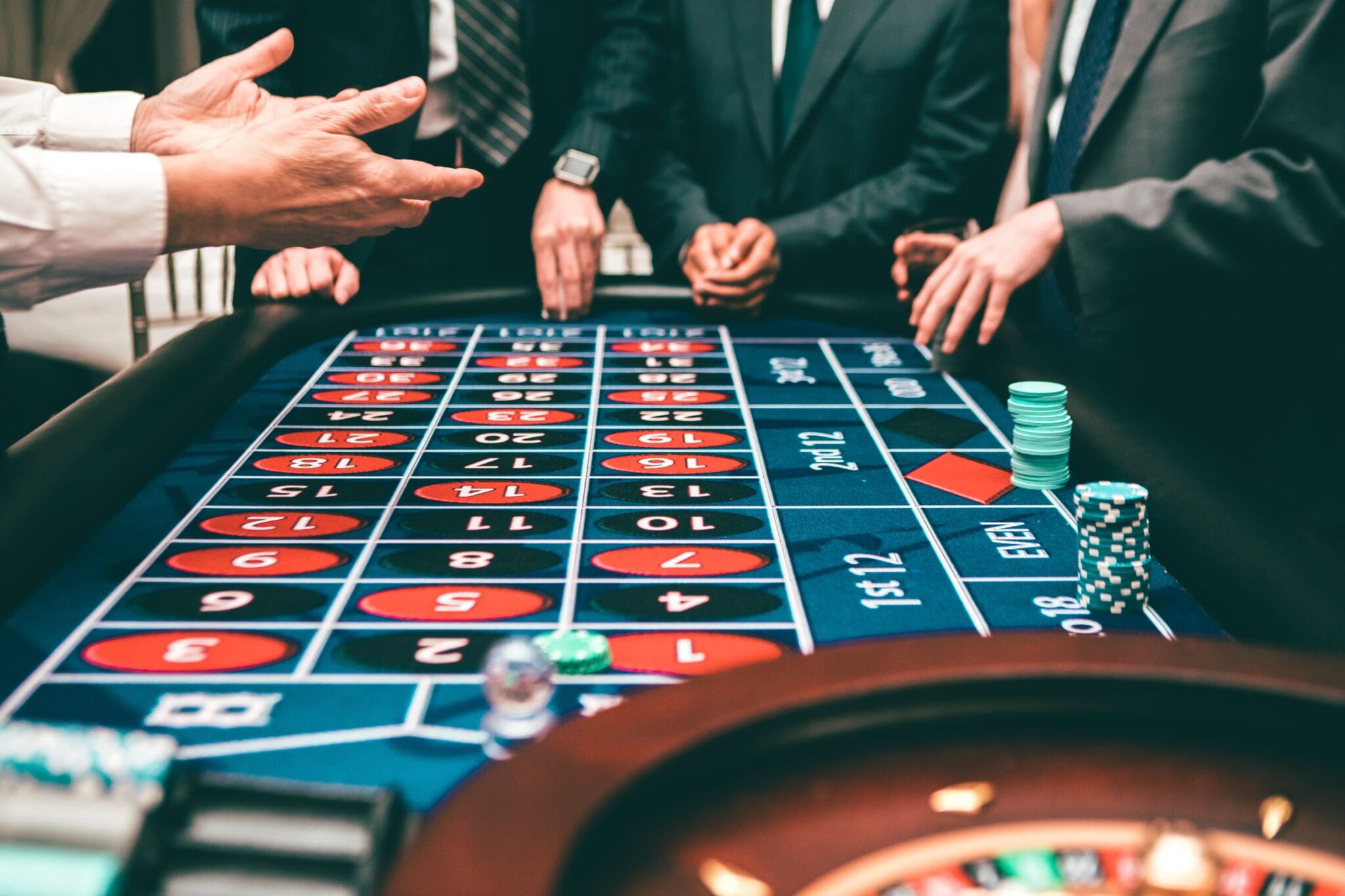 Mężczyźni w garniturach, stojący przy stole, w kasynie, przy żetonach i kartach
