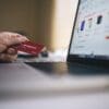 Ręka trzymająca kartę płatniczą przy ekranie komputra, z otwartą stroną e-commerce