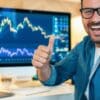 Trader pokazujący gest kciuka w górze, lapotp, wykresy, logo Algotech