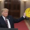 Donald Trump trzymający w dłoni dużą złotą monetę Ethereum