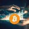 Bitcoin, w tle ręce trzymające wykres giełdowy pokazujący wzrost.