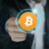 Dłoń wskazująca na monetę Bitcoin.