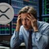 Zdezorientowany trader trzymający się za głowę. W tle wykresy giełdowe i logo Ripple (XRP).