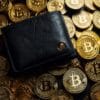 Czarny portfel leżący na stercie Bitcoinów.
