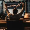 Trader w fotelu przed monitorem komputera świętuje sukces. Na monitorze widać wykresy giełdowe.