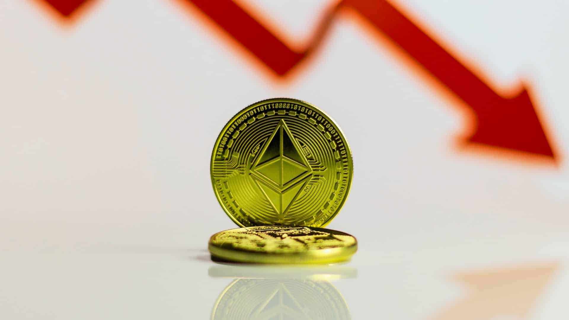 Złota moneta Ethereum na lśniącym blacie, w tle czerwona strzałka sugerująca spadek wartości.