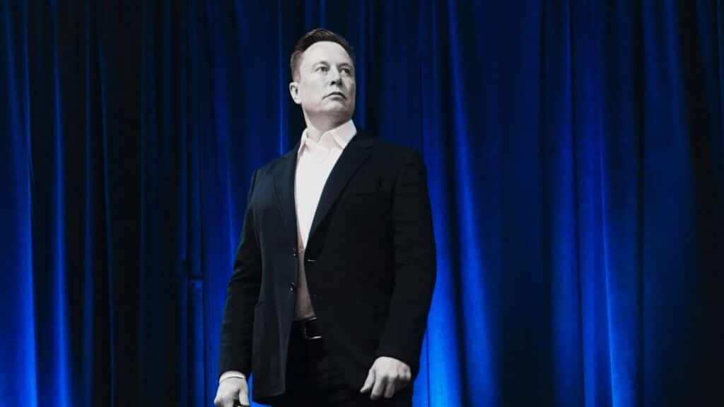 Zamyślony Elon Musk na granatowym tle.