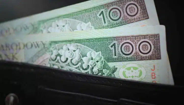 Dwa banknoty 100 zł w wystające z czarnego portfela.