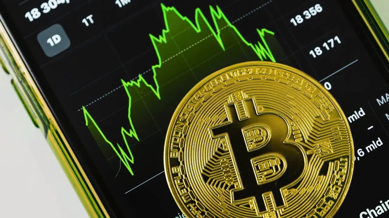 Bitcoin na tle smartfona, kt&oacute;ry wyświetla wykres wzrostu.