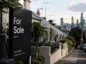 Domy wystawione na sprzedaż na australijskim rynku nieruchomości, z tablicą „For Sale” na pierwszym planie i zabudową miejską w tle, symbolizujące spowolnienie sprzedaży mieszkań.