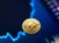 Złota moneta Bitcoin na tle rosnącego, wyblakłego wykresu. Kolorystyka niebieska i ciemnoniebieska.