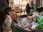 Mężczyzna wyciąga plastikowe butelki i puszki z ulicznego pojemnika w Lizbonie, a w tle widać automat do zwrotu opakowań.