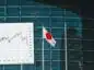 Budynek banku z widoczną flagą Japonii i wykresem jena do dolara amerykańskiego