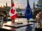 Flagi Kanady i Unii Europejskiej stoją na stole negocjacyjnym na tle miasta, symbolizując zacieśnianie współpracy gospodarczej między Kanadą a UE.