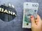 Bank na tle dłoni trzymającej polskie banknoty.