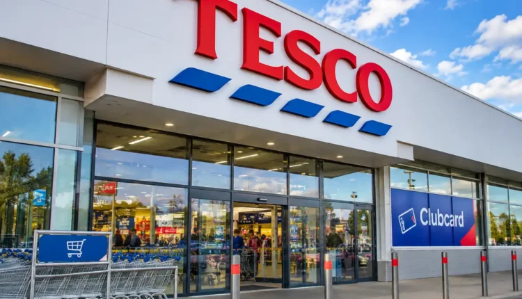 Wejście do sklepu Tesco z charakterystycznym czerwonym logo i rzędami wózków zakupowych przed budynkiem. Grafika ilustruje sprzedaż działalności Tesco w Czechach i na Słowacji holenderskiej grupie Ahold Delhaize.